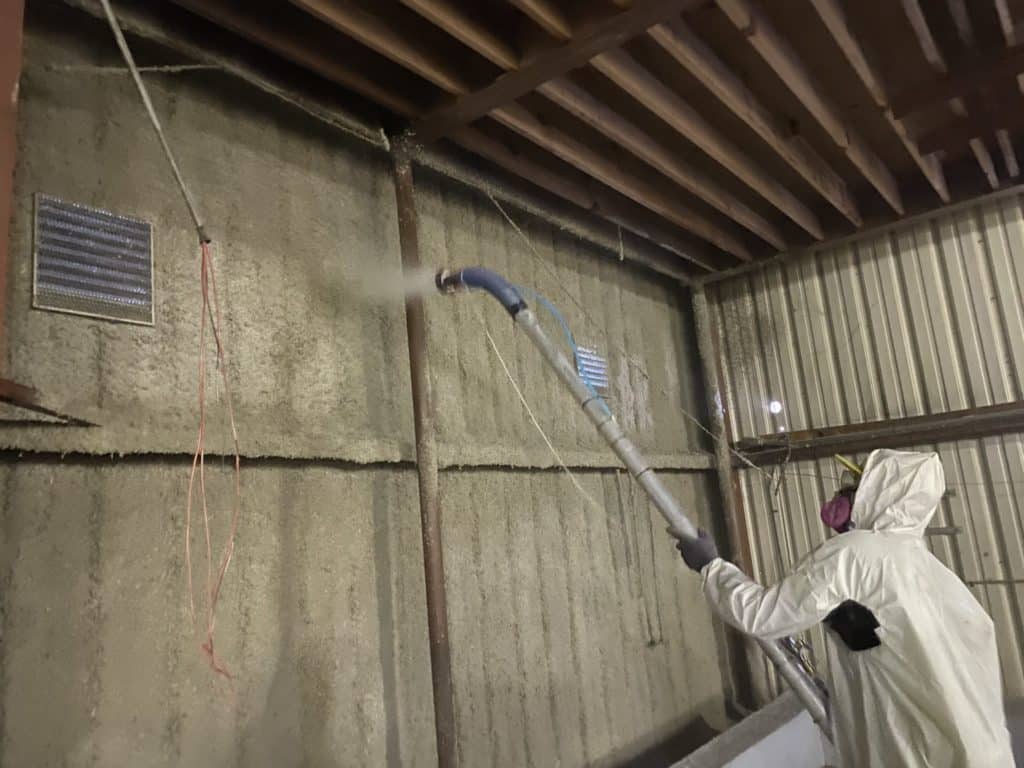 Fireproofing material being applied in a spray application to a metal building