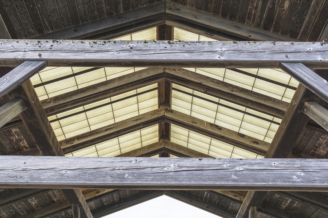 Looking up from inside a hot attic at the wooden rafters and roof sheathing, with intense sunlight filtering through the gaps, illustrating how the roof radiates heat into a home.