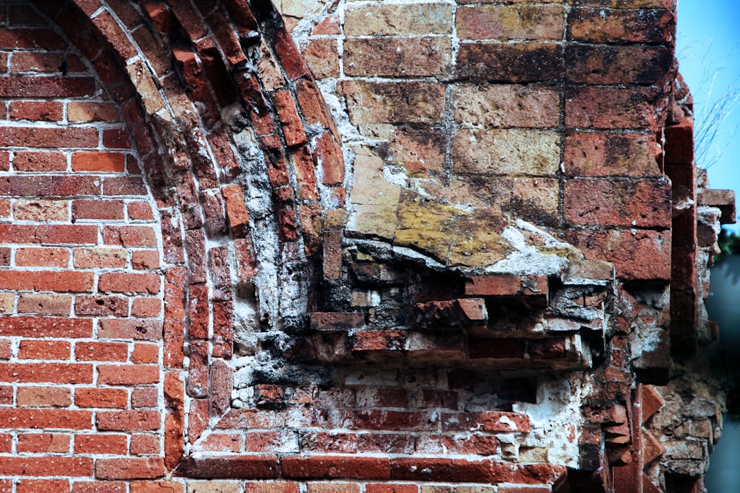 A construction worker pulling out old, wet, and sagging insulation from between the wooden studs of a flood-damaged wall during demolition.