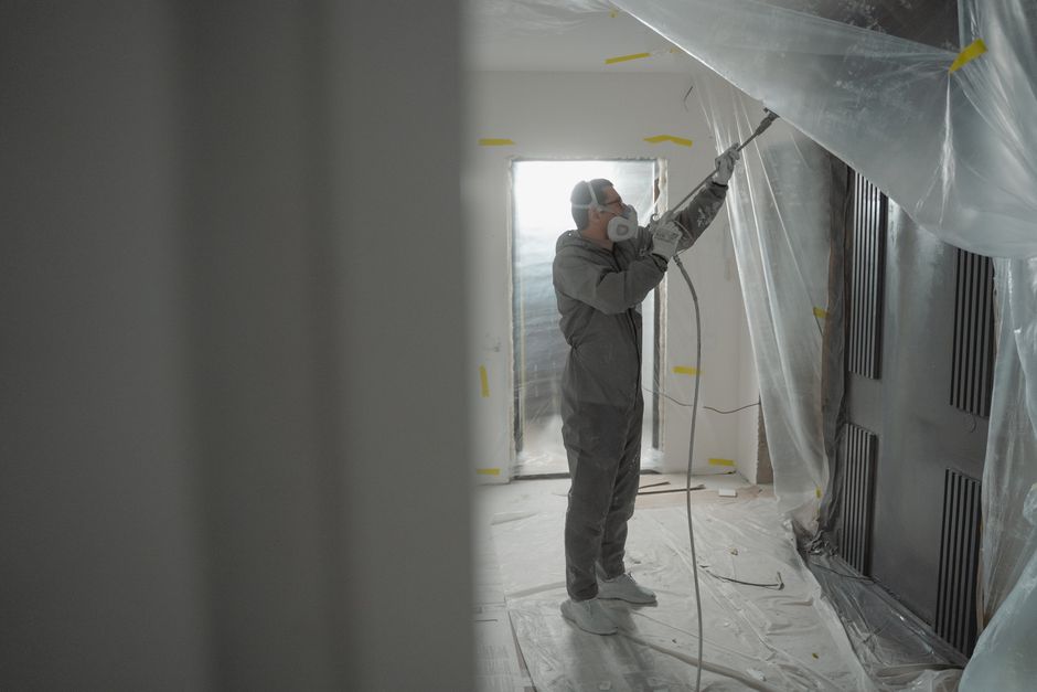 Professional contractor in protective gear is carefully applying expanding spray foam insulation to the underside of a res...