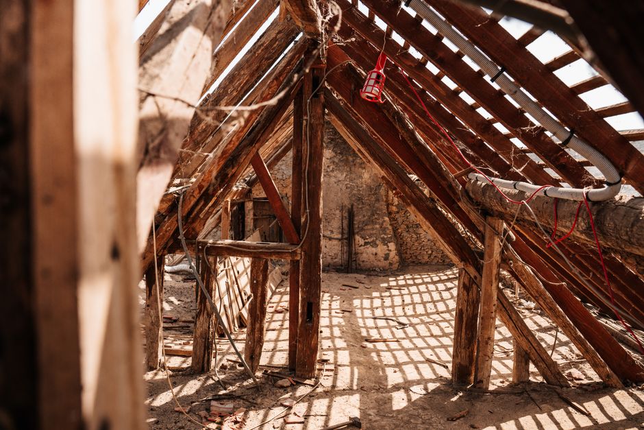 A close-up view of old, dusty, and deteriorating pink fiberglass insulation in a dark and moody attic, highlighting the hidden structural risks in a home.