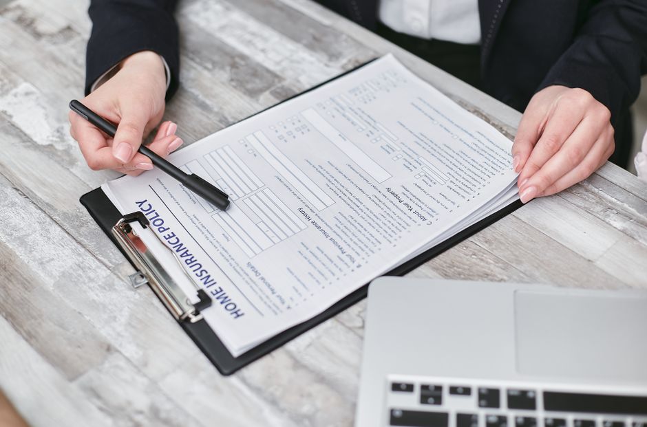 A homeowner sits at a desk with their head in their hands in frustration while holding an official insurance denial letter, representing financial stress.