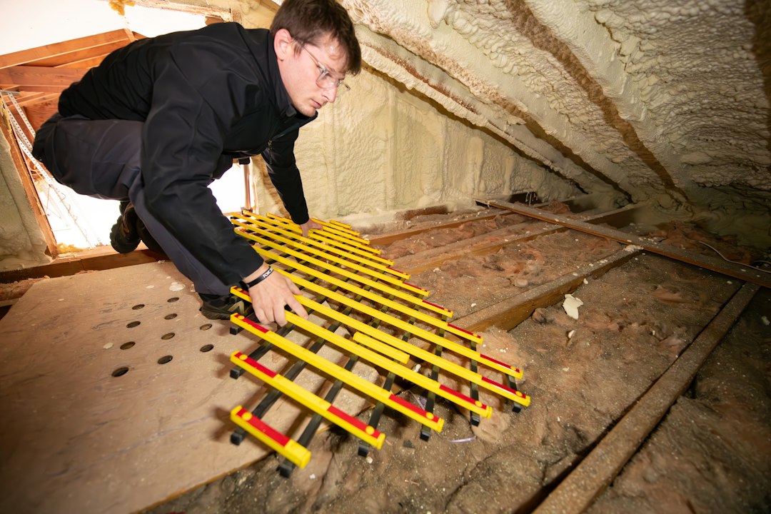A professional contractor in protective gear applying spray foam insulation to the rafters and ceiling of a residential attic.