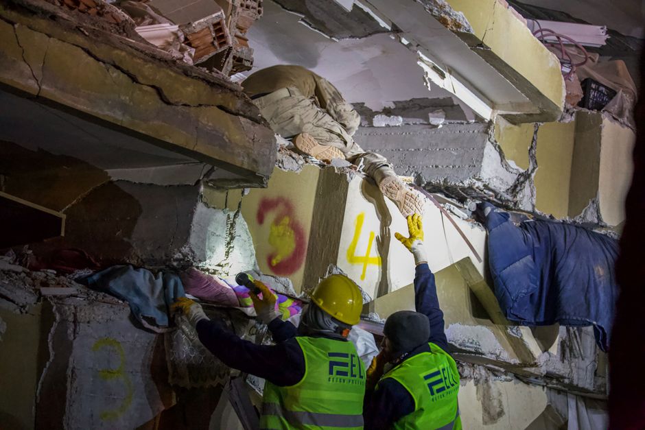 A professional in protective gear tearing out a section of water-damaged drywall, revealing the costly remediation process for hidden mold and rot.