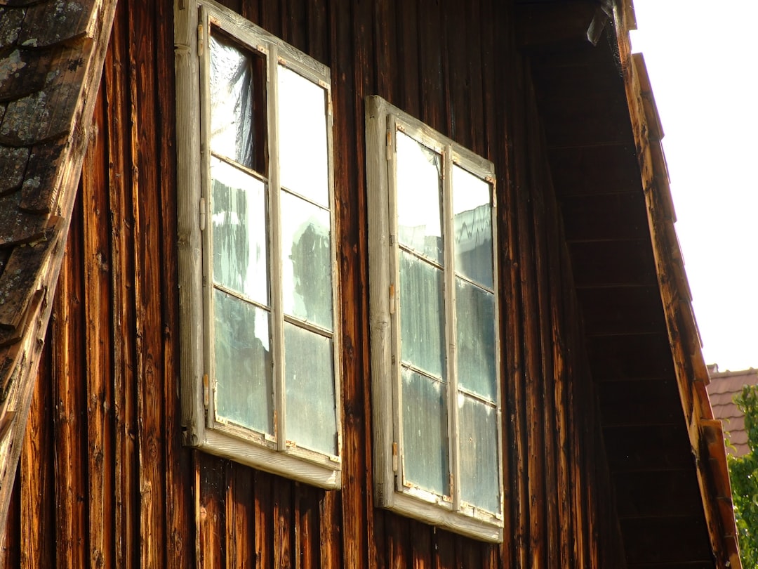 Sunlight streams through the old, weathered wooden rafters of a dark attic, highlighting the structural bones of a house in need of proper insulation.