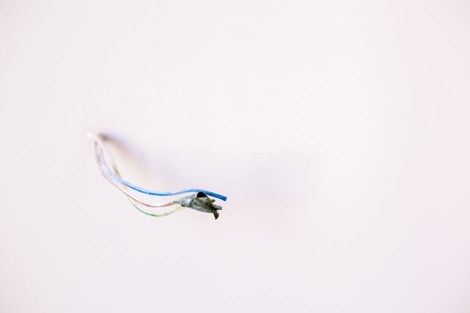 The aftermath of an electrical fire, showing a melted and charred electrical outlet on a blackened, burnt wall, symbolizing the dangers of faulty wiring.