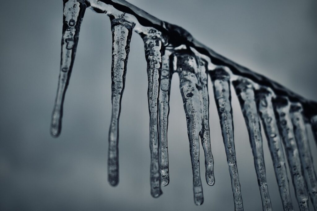 Close-up photograph of a residential air conditioning unit with ice built up on the coils and fins, dripping water, symbol...