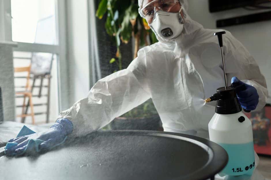 A professional insulation contractor wearing a full white protective suit and mask removing old insulation from a residential attic.
