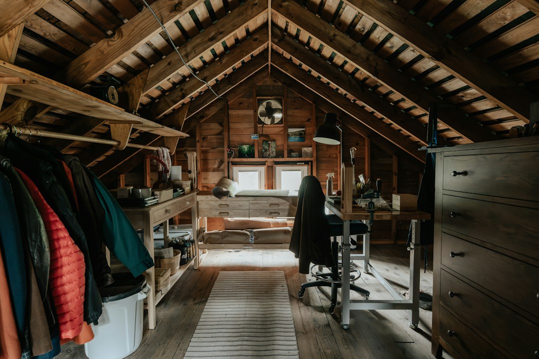 Sunlight streams through a vent into a hot, dusty, unfinished attic with exposed wood beams, evoking the uncomfortable heat of a Louisiana summer.
